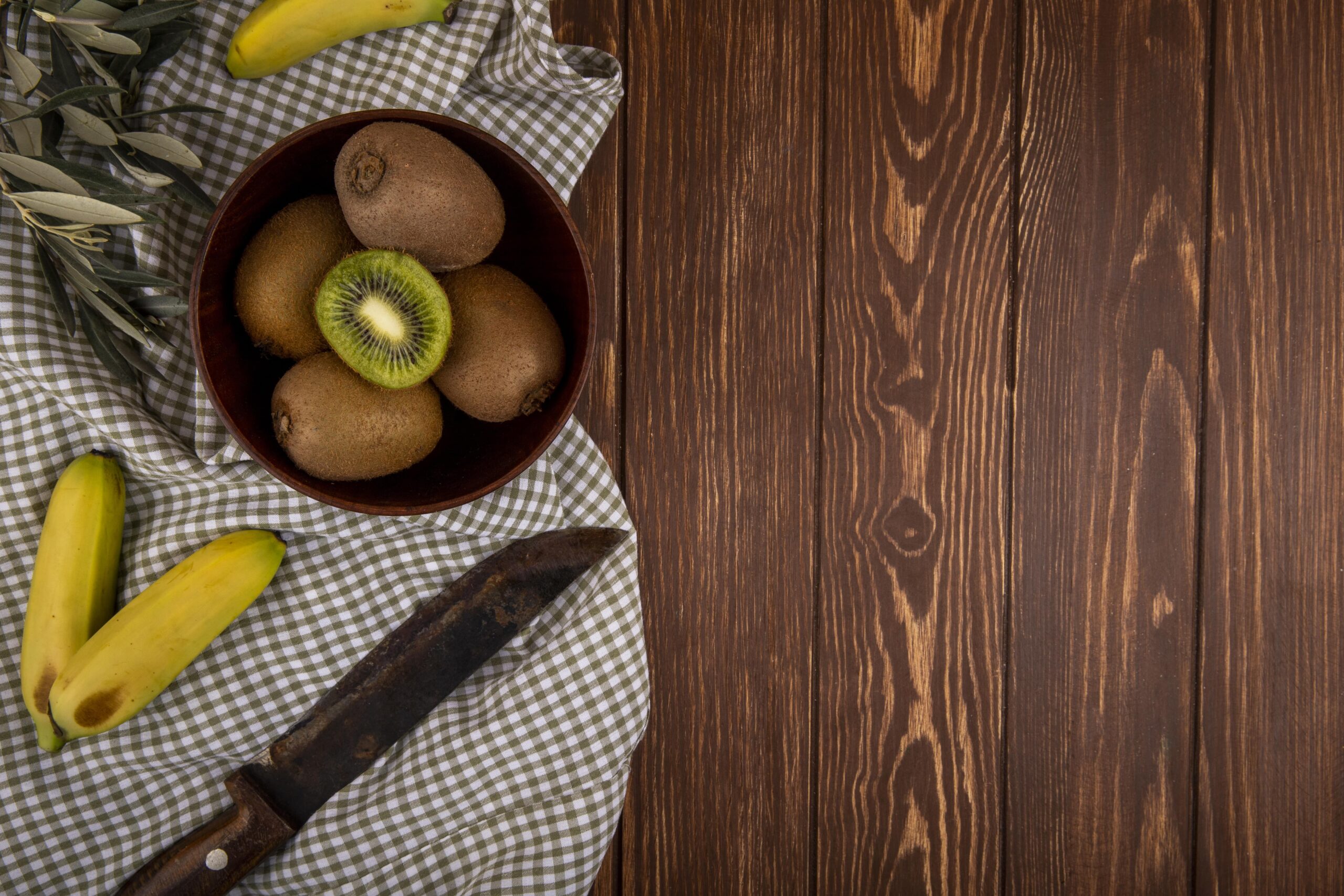 top-view-fresh-kiwi-fruit-wooden-bowl-fresh-bananas-with-old-kitchen-knife-rustic-with-copy-space-min